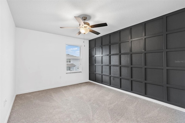 carpeted empty room with a decorative wall, baseboards, and a ceiling fan