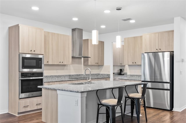 33263 Sycamore Leaf Dr, Wesley Chapel, FL 33545 - kitchen featuring stainless steel appliances, wall chimney range hood, light brown cabinetry, a sink, and a kitchen island with sink