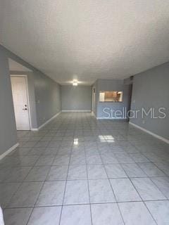 empty room with a textured ceiling, tile patterned flooring, and baseboards