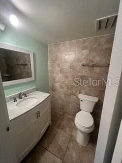 bathroom featuring vanity, tile walls, toilet, tile patterned flooring, and visible vents