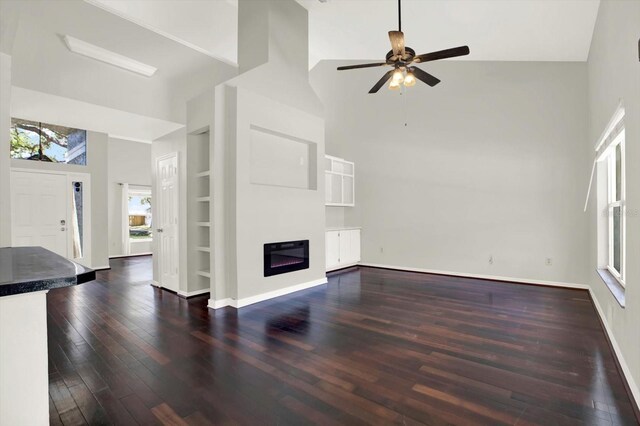 9603 Sunnyoak Dr, Riverview, FL 33569 - unfurnished living room featuring a glass covered fireplace, a towering ceiling, built in features, a ceiling fan, and dark wood-type flooring