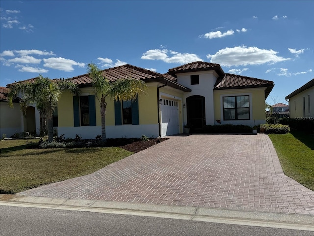 mediterranean / spanish home with a garage, decorative driveway, stucco siding, and a front lawn