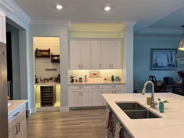 kitchen featuring a sink, wine cooler, crown molding, light wood-style floors, and white cabinetry