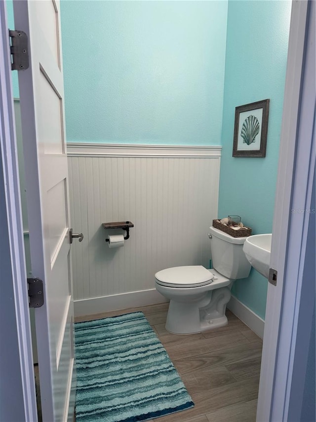 half bathroom featuring toilet, wood finished floors, wainscoting, baseboards, and wooden walls