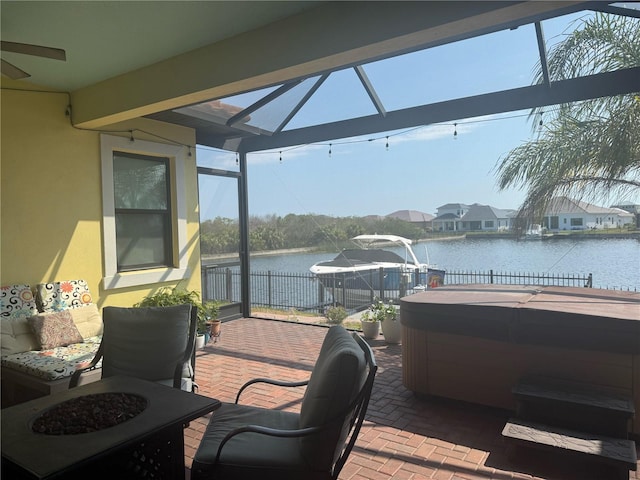 deck featuring a hot tub, a patio area, a water view, and fence