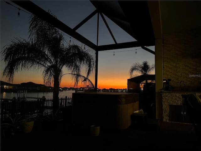 view of patio featuring a hot tub, fence, and a water view