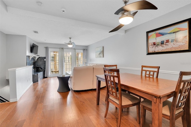 dining space with a ceiling fan, light wood-style floors, visible vents, and a fireplace