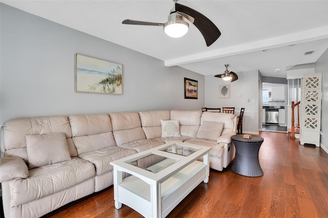 living room with a ceiling fan, visible vents, beam ceiling, and dark wood-style flooring