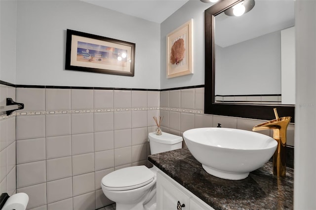 bathroom with toilet, vanity, a wainscoted wall, and tile walls