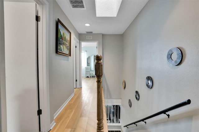 hallway featuring light wood-type flooring, baseboards, a skylight, and visible vents