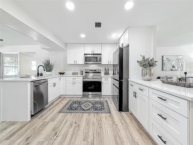1469 S Hillcrest Ave, Clearwater, FL 33756 - kitchen with stainless steel appliances, a peninsula, white cabinetry, light wood-type flooring, and recessed lighting