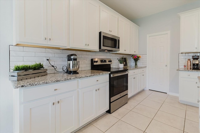 kitchen with tasteful backsplash, appliances with stainless steel finishes, white cabinetry, light stone countertops, and light tile patterned flooring