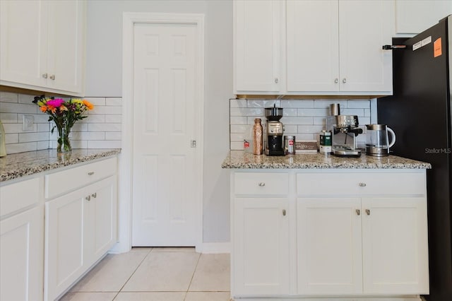 kitchen featuring tasteful backsplash, light tile patterned floors, freestanding refrigerator, white cabinetry, and light stone countertops