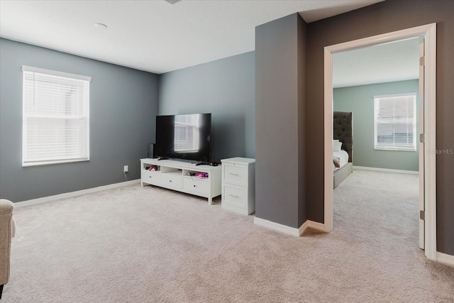 living area featuring light carpet, baseboards, and plenty of natural light
