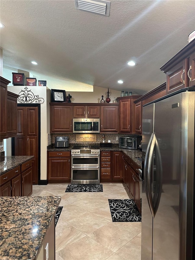 kitchen featuring backsplash, a textured ceiling, visible vents, appliances with stainless steel finishes, and vaulted ceiling