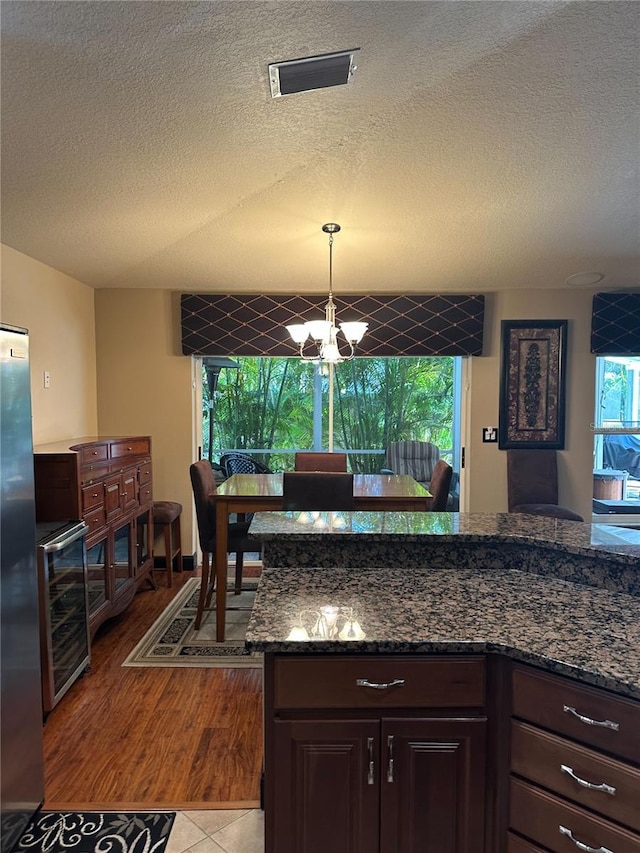 kitchen with an inviting chandelier, beverage cooler, a textured ceiling, freestanding refrigerator, and visible vents
