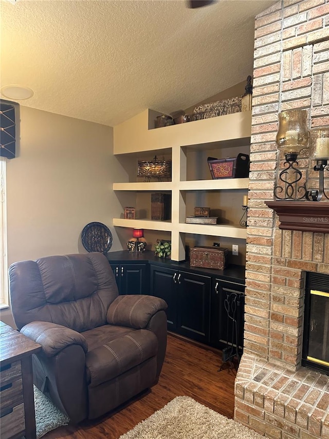 living area featuring a brick fireplace, a textured ceiling, and wood finished floors