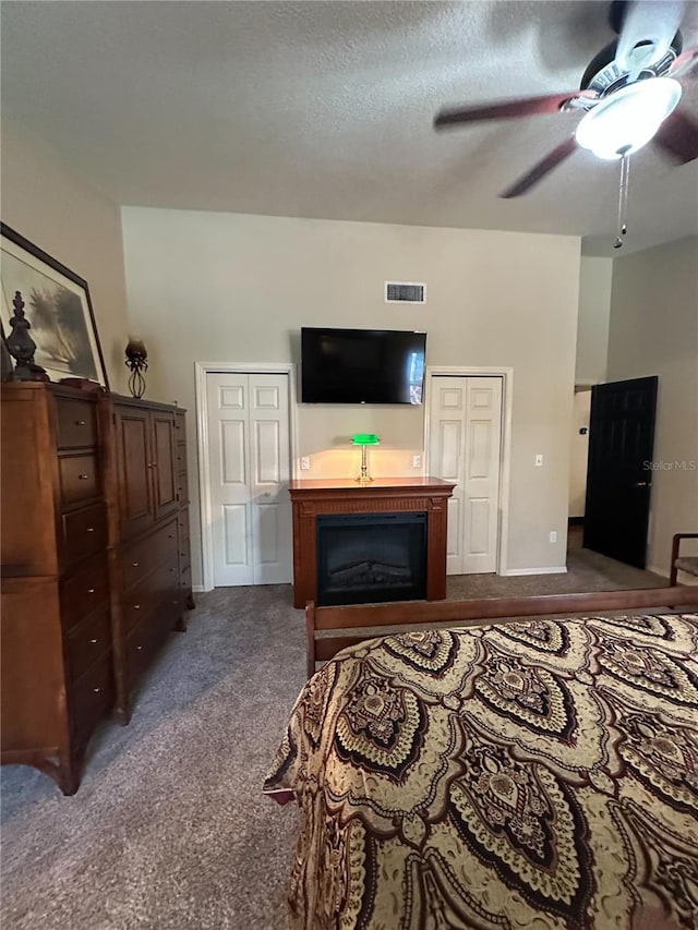 bedroom featuring visible vents, baseboards, dark colored carpet, a textured ceiling, and a ceiling fan
