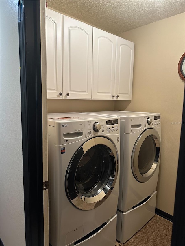 clothes washing area with a textured ceiling, washing machine and dryer, and cabinet space