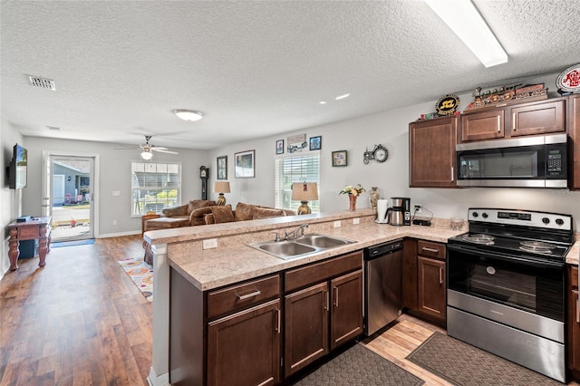 6745 Basswood Cir, Zephyrhills, FL 33542 - kitchen featuring a sink, appliances with stainless steel finishes, a peninsula, a textured ceiling, and light wood-style flooring