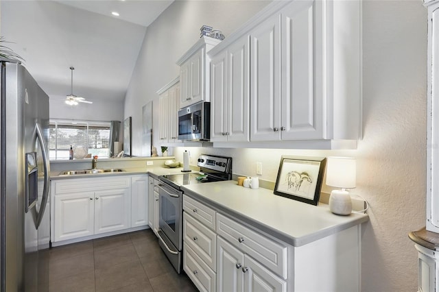 kitchen with a sink, white cabinetry, stainless steel appliances, dark tile patterned flooring, and lofted ceiling