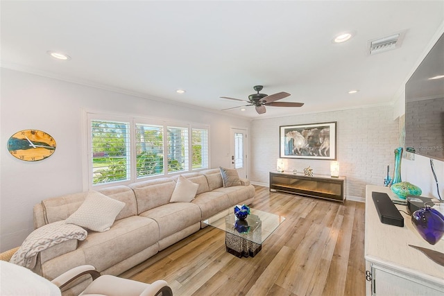 living room with a ceiling fan, ornamental molding, visible vents, brick wall, and light wood finished floors