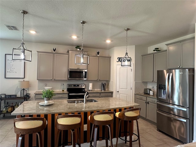 33034 Sand Creek Dr, Wesley Chapel, FL 33543 - kitchen with appliances with stainless steel finishes, gray cabinetry, backsplash, light stone counters, and a breakfast bar area