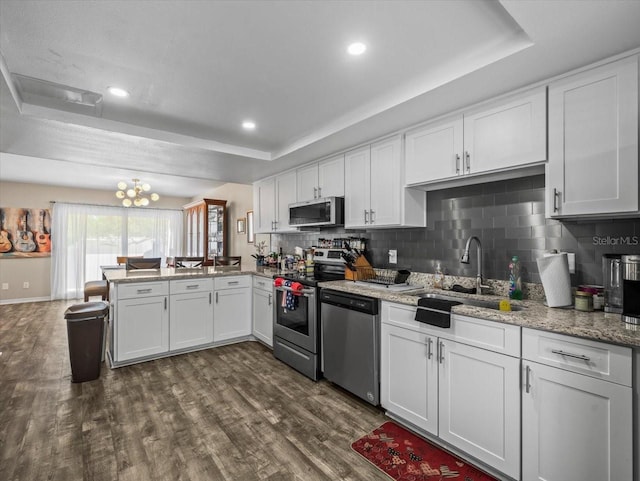 kitchen featuring dark wood-style flooring, a peninsula, backsplash, appliances with stainless steel finishes, and a sink
