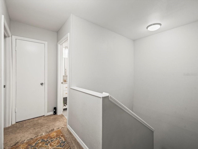 hall featuring carpet floors, baseboards, and an upstairs landing
