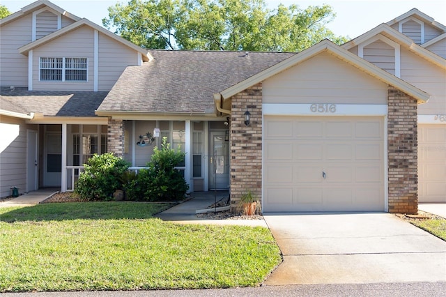 view of front facade with a front lawn, driveway, a shingled roof, a garage, and brick siding