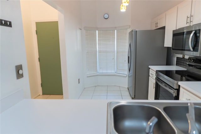 kitchen with a sink, light tile patterned floors, white cabinetry, light countertops, and appliances with stainless steel finishes