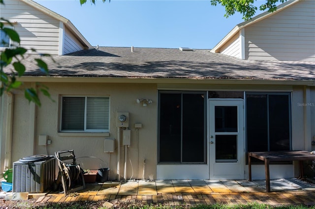 view of exterior entry with cooling unit, a patio area, and a shingled roof