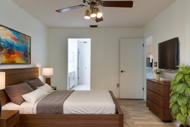bedroom with a textured ceiling, light wood-type flooring, visible vents, ceiling fan, and ensuite bath