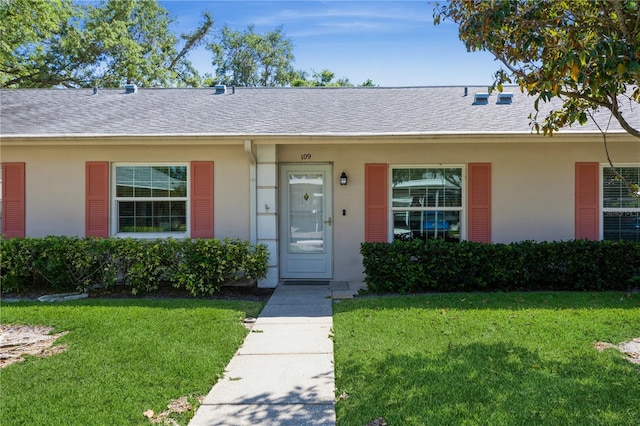 view of front of property with a shingled roof, a front lawn, and stucco siding