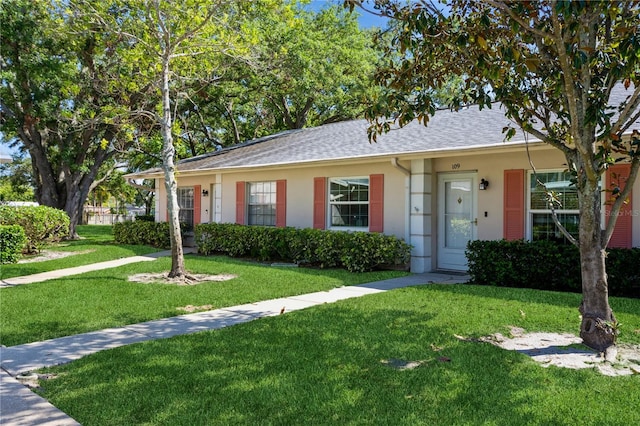 ranch-style home featuring a shingled roof, a front lawn, and stucco siding
