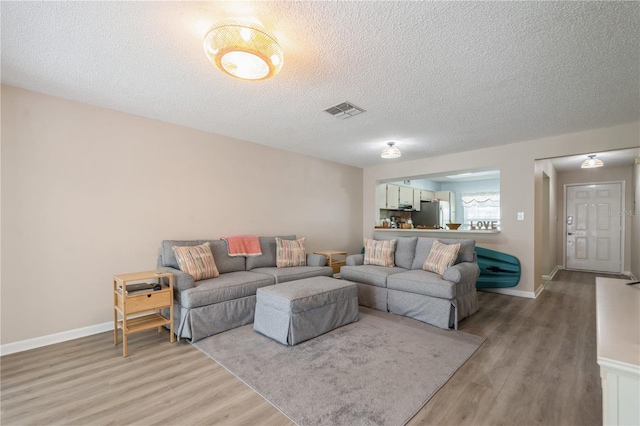 living room featuring baseboards, light wood-style flooring, visible vents, and a textured ceiling