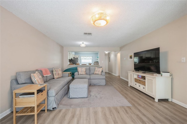 living area featuring a textured ceiling, light wood-style flooring, visible vents, and baseboards