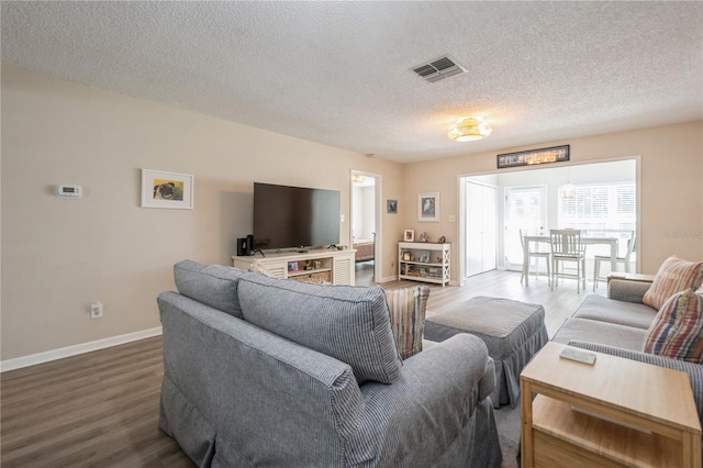 living area with a textured ceiling, wood finished floors, visible vents, and baseboards