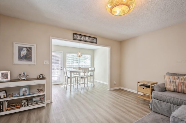 living area featuring wood finished floors, a textured ceiling, baseboards, and an inviting chandelier