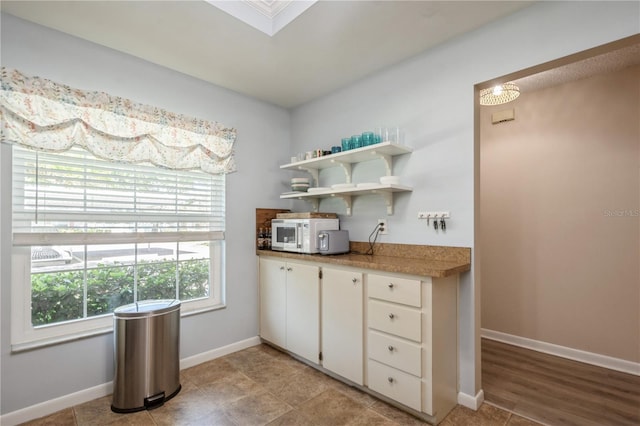 kitchen with white cabinets, open shelves, light countertops, baseboards, and white microwave