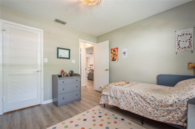 bedroom featuring a textured ceiling, light wood-type flooring, visible vents, and baseboards
