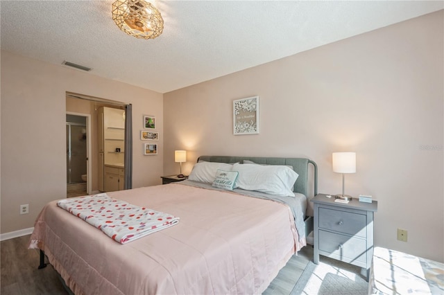 bedroom with baseboards, wood finished floors, visible vents, and a textured ceiling