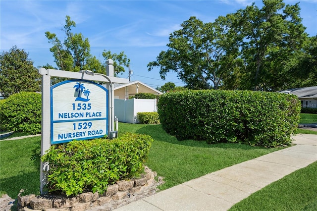 community / neighborhood sign featuring a lawn and fence