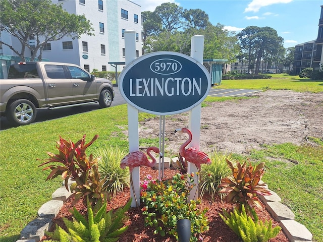 community / neighborhood sign featuring uncovered parking and a lawn