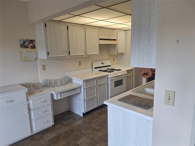 kitchen with tasteful backsplash, a sink, light countertops, under cabinet range hood, and white gas stove
