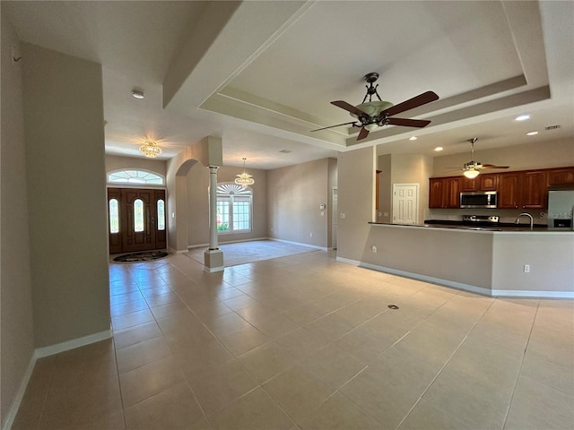 1201 Ventana Dr, Sun City Center, FL 33573 - unfurnished living room featuring a raised ceiling, arched walkways, light tile patterned flooring, and ceiling fan with notable chandelier
