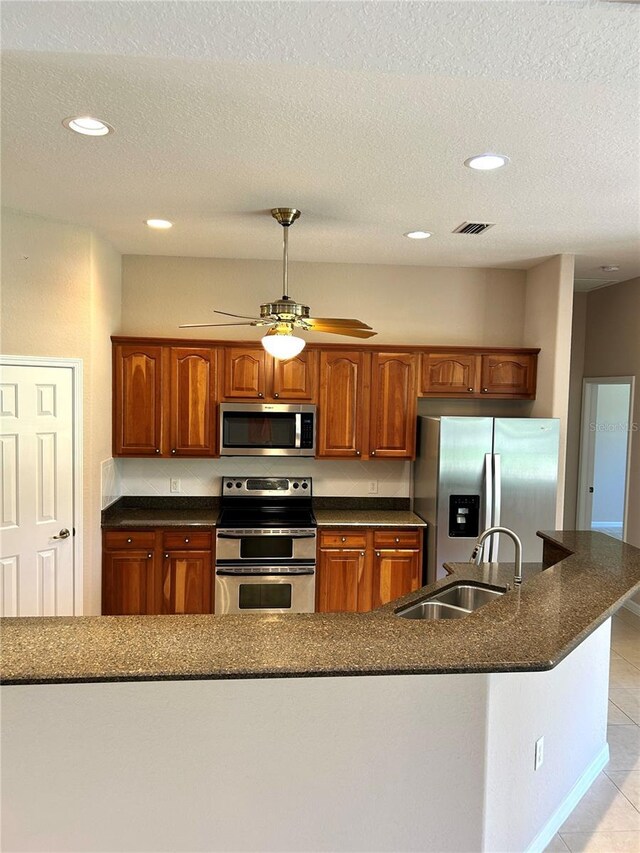 1201 Ventana Dr, Sun City Center, FL 33573 - kitchen with light tile patterned floors, a ceiling fan, a sink, stainless steel appliances, and brown cabinets