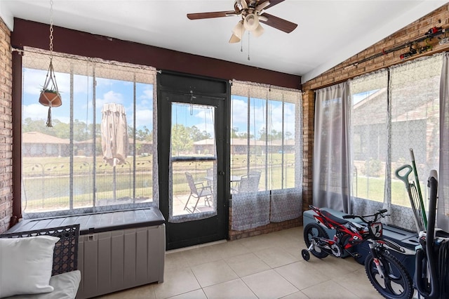 sunroom / solarium featuring brick wall, lofted ceiling, plenty of natural light, and tile patterned flooring
