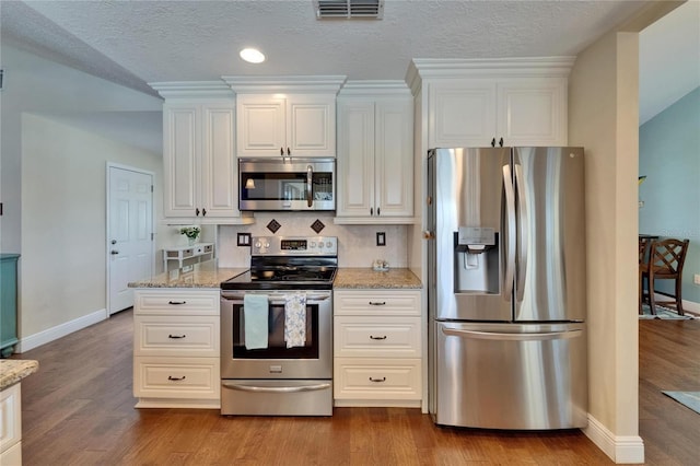 907 Golf Island Dr, Apollo Beach, FL 33572 - kitchen featuring appliances with stainless steel finishes, baseboards, wood finished floors, light stone counters, and a textured ceiling