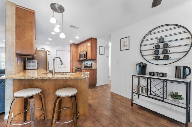 kitchen featuring stainless steel appliances, a sink, brown cabinets, decorative backsplash, and light stone countertops
